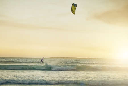 Catching some waves. Rearview shot of a young woman kitesurfing at the beach.の写真素材