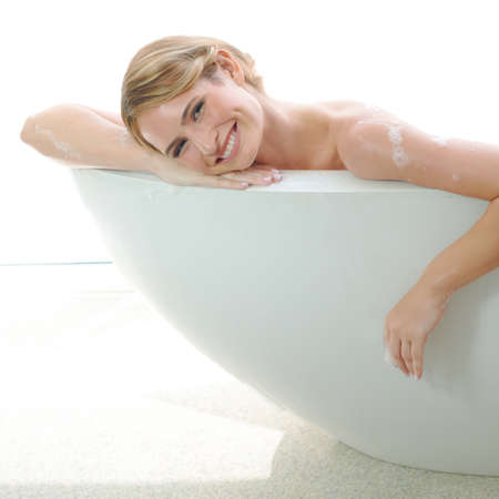 She enjoys pampering herself. A beautiful young woman smiling at you while enjoying a luxurious bath.の写真素材