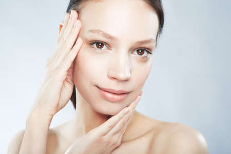 Flawless femininity. Head and shoulder portrait of a beautiful young woman in the nude posing with and hands on her face.の写真素材