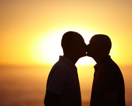 Blissful sunset kiss - Gay Couple. Sihlouette portrait of homosexual couple kissing in front of a sunset - copyspace.の写真素材