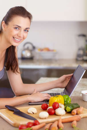 Checking the internet for a good recipe. Portrait of a beautiful young woman looking for recipes on her digital tablet while cooking.の写真素材