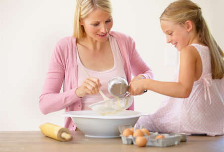 Mixing it all in with mum. A little girl sitting on a kitchen counter and helping her mother bake.