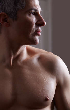 Sculpted and thoughtful. A darkly lit image of a shirtless man looking away thoughtfully.の写真素材
