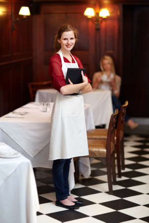 How may I serve you. Cute young waitress standing waiting to serve a customer - portrait.の写真素材
