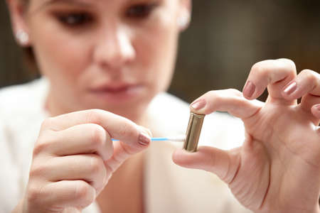Residue might reveal the criminal. A forensic scientist applying an ear bud to a bullet.