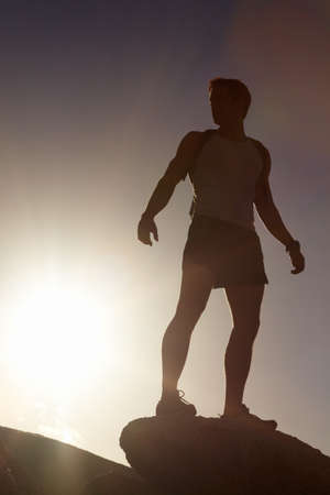 Living a life of adventure. A silhouette of a man standing atop a cliff.の写真素材