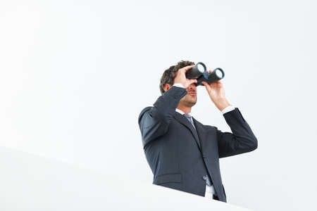 Visionary business man. Low angle view of handsome business man looking through binoculars.の写真素材