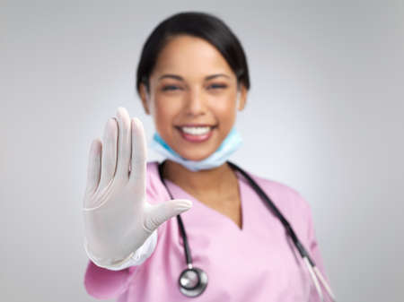 Stop covid in its tracks. Cropped portrait of an attractive young female healthcare worker gesturing stop while standing in studio against a grey background.の写真素材