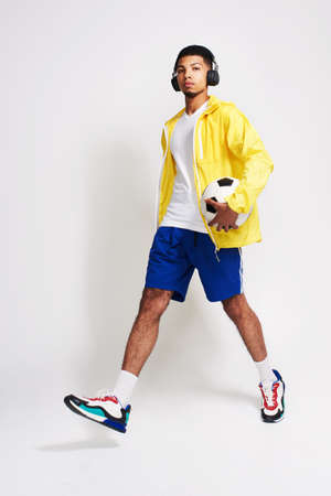 He has that soccer feelings. Portrait of a handsome young man listening to music while holding a soccer ball inside of a studio.の写真素材