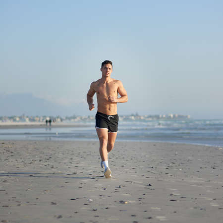 Making tracks. Full length shot of a handsome young man running on the beach.