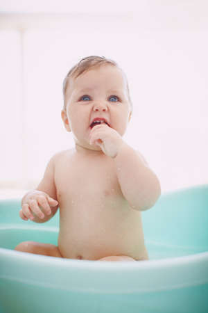 Im definitely clean now. A cute baby girl sitting happily in the bathtub.の写真素材