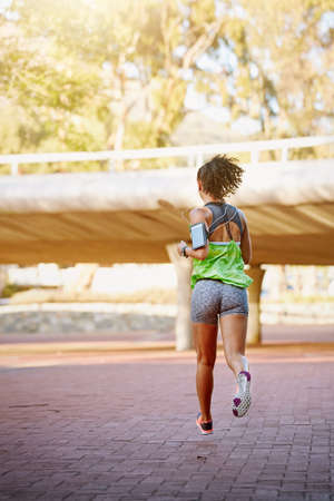 Out on her daily jog. Rear view shot of a sporty young woman out for a run.の写真素材