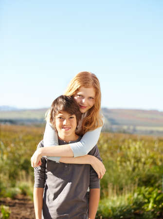 Sisterly love. Portrait of a young boy giving his sister a piggyback in the garden.の写真素材
