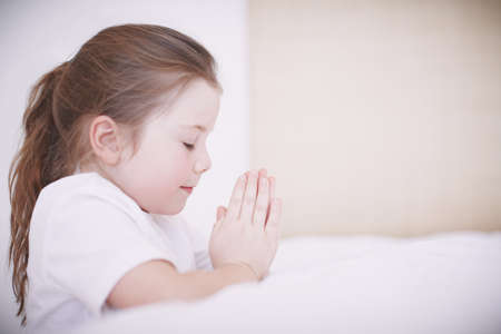 Thank you God for everything. Side view of a young girl kneeling by her bed and saying her prayers.の写真素材