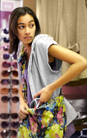 The shoplifter sale is on. Cropped shot of a young woman sneaking stolen clothing into her handbag.