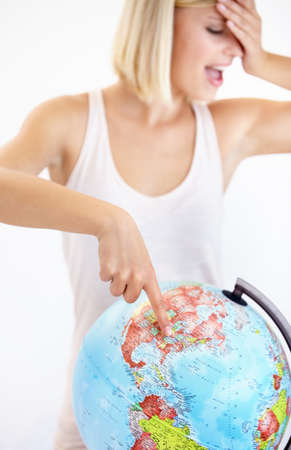 Travelling is her passion. A pretty young woman covering her eyes and pointing at her next destination on a globe.の写真素材