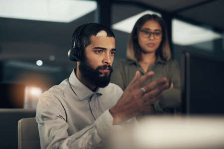 I could use your help to figure this one out. Shot of a call centre agent working in an office alongside a colleague at night.の写真素材