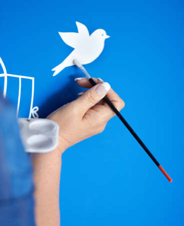 Creativity in flight. Closeup of a female artist painting a bird on a blue background.の写真素材