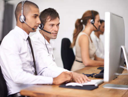 Have you turned it off and back on again. Shot of a group of help desk operators wearing headsets and working in an office.の写真素材