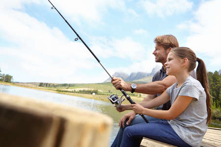 Shes already an expert angler. Shot of a father showing his daughter how to fish.の写真素材