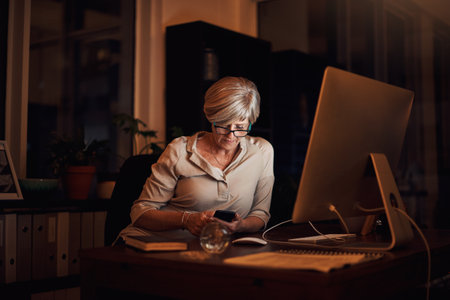 It may be late, but shes still reachable. Cropped shot of an attractive mature businesswoman sending a text while working late in her office.の写真素材