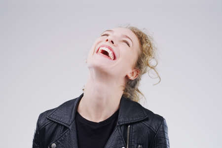 Live a little. Laugh a lot. Studio shot of an attractive young woman laughing while standing against a grey background.の写真素材