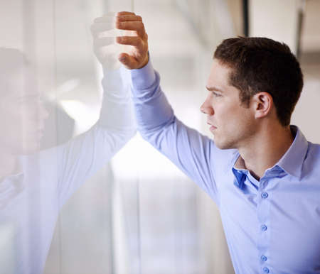 What does my future hold. A young businessman standing against a glass wall looking worried.の写真素材