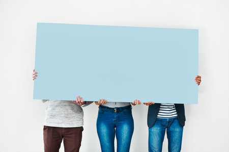 Your space with a bit of blue. Studio shot of a group of people covering themselves with a blank placard against a white background.の写真素材