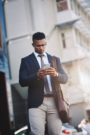 Making business moves straight from his device. Shot of a handsome young businessman using a cellphone in the city.の写真素材