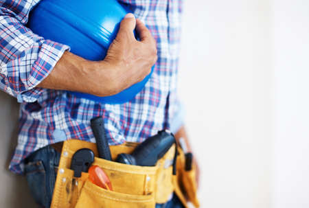 Construction worker holding protective helmet. Mid section of construction worker with tool belt holding blue protective helmet.の写真素材