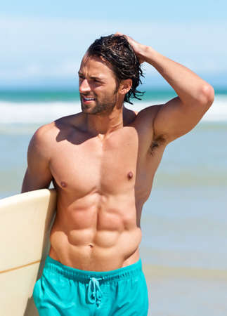 Surfing keeps him in great shape. An attractive young man heading to the water with his surfboard.