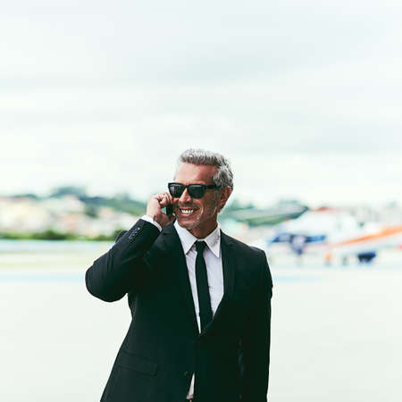 Ill see you soon. Cropped shot of a handsome mature businessman talking on his cellphone while walking outside of the airport.の写真素材