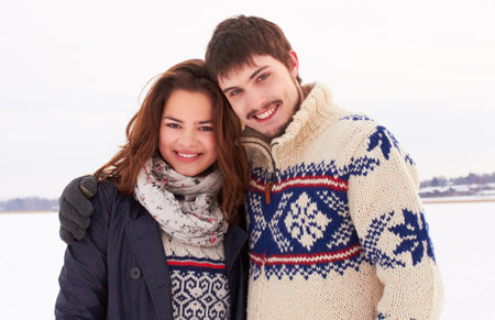 Warm cuddles on a winters day. Shot of a sweet young couple outdoors in the snow.の写真素材