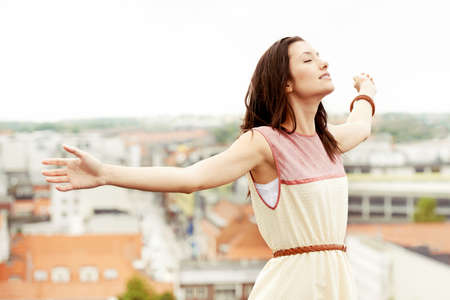 Letting go and feeling free. Gorgeous young woman standing on a rooftop with her arms outstretched.の写真素材
