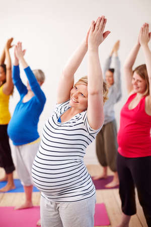 Keeping limber during pregnancy. A multi-ethnic group of pregnant women doing exercises with their arms stretched upwards.の写真素材
