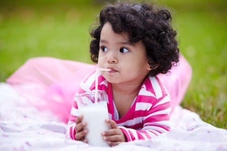 Mmmmm. Adorable little girl drinking milk through a straw while lying on the grass.の写真素材