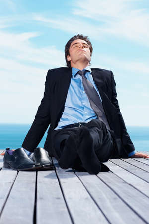 Young business man enjoying the sun on a wooden pier. Young relaxed business man enjoying the sun on a wooden pier.の写真素材