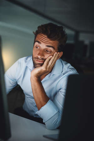 Things suddenly turned very slow and dull. Shot of a young businessman looking bored while working late in an office.の写真素材