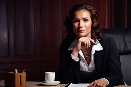 Qualified to give expert advice. Attractive mature legal woman sitting and leaning on her hand while smiling slightly at the camera.の写真素材