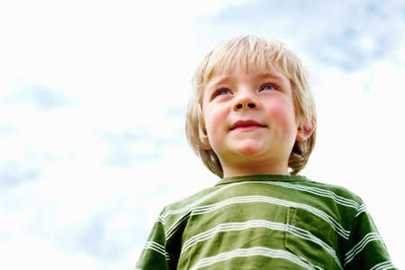 Cute young boy smiling. Low angle view of cute young boy standing against sky and smiling.の写真素材
