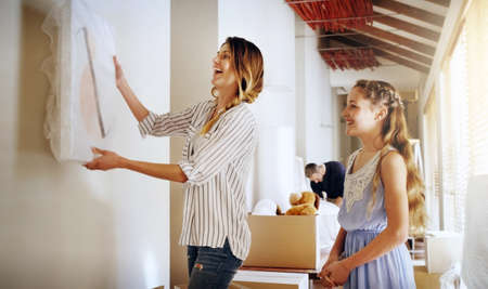 Well hang your painting right here. Shot of a mother and her daughter deciding where to hang a frame in their new house.の写真素材