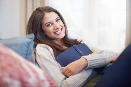 A young woman lying on the couch with a book. Relaxing with her favorite book.
