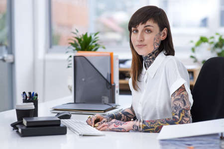 Exercising self-expression. A shot of a tattooed businesswoman sitting at her desk in her office.の写真素材