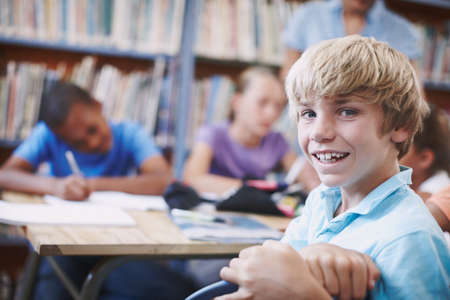 Im making so many friends. An excited young boy sitting in the library with his classmates.の写真素材