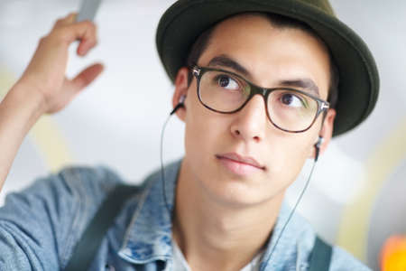 Music on the go. Young guy taking public transport while listening to his mp3 player.の写真素材