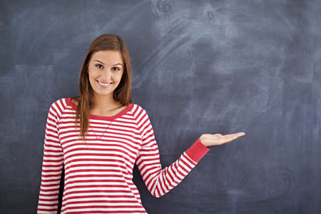 May I direct your attention right here. Portrait of a gorgeous young woman standing in front of a blackboard.の写真素材