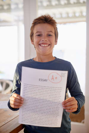Check this out. Shot of a proud young boy holding up his essay that got him an A+.の写真素材