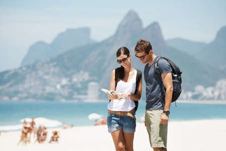 Getting our bearings in paradise. Shot of a young couple looking at a map while standing on a beach.の写真素材