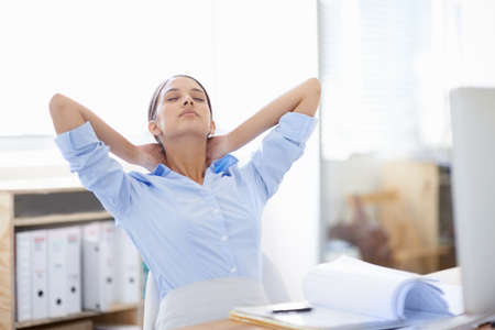Stretching those tight neck muscles. Shot of young businesswoman taking a moment to relax at her desk.の写真素材