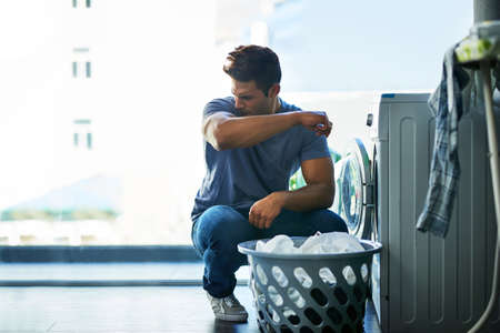 That doesnt smell good, this needs to be washed too. Shot of a young man doing household chores.の写真素材